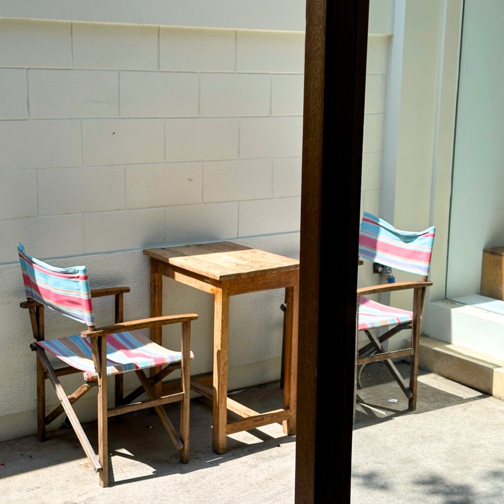Two striped folding chairs and a small wooden table in a sunlit courtyard