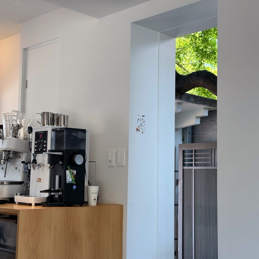 Espresso machine and grinder on a wooden counter beside a doorway to a leafy courtyard