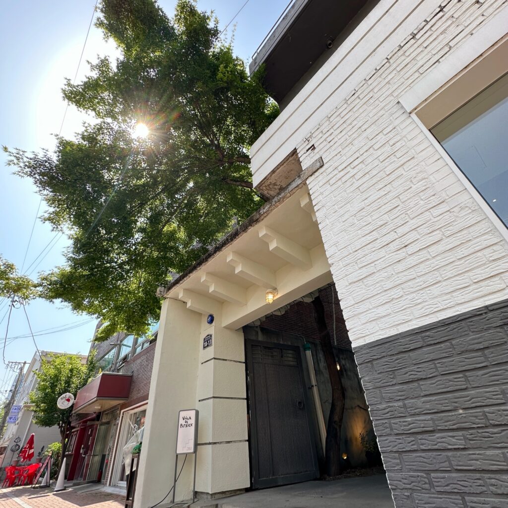 White brick house with a gray gate and the Villa de Patrick sign under a tall maple tree