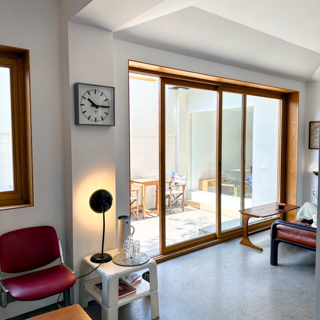 Sunny seating area with a wall clock, a black desk lamp, and a sliding glass door to the courtyard
