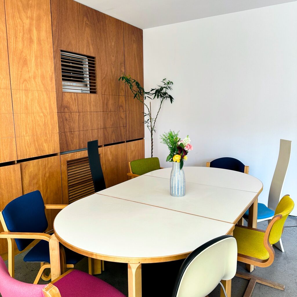 Oval white table with colorful chairs and a vase of flowers in front of a wood-paneled wall