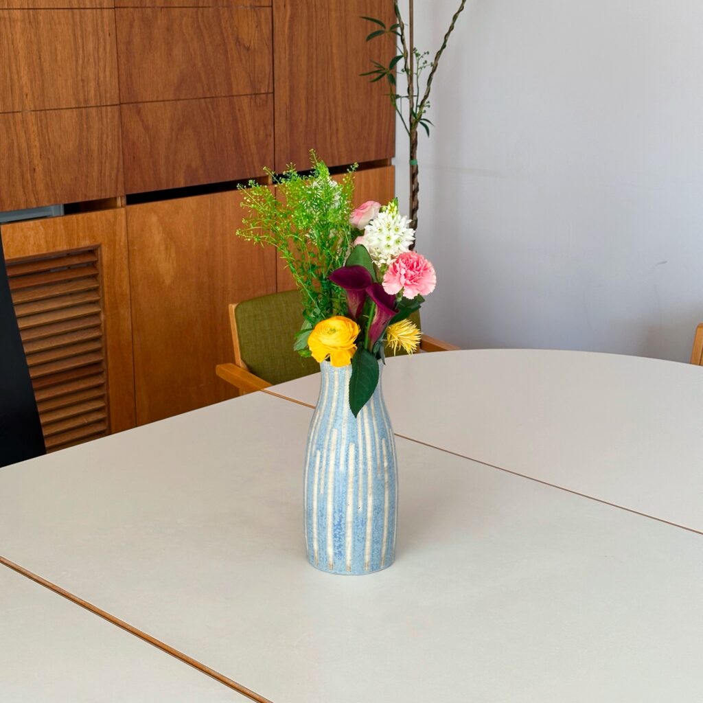 A blue striped ceramic vase with yellow ranunculus, pink carnations, and calla lilies
