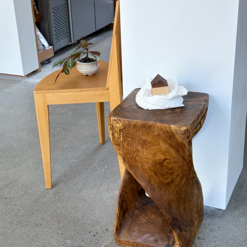 A twisted wooden stool with napkins beside a wooden chair holding a small potted plant