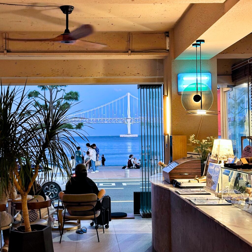 Inside the café with its front wide open to the beach, Gwangan Bridge in the distance, a long counter, a pendant lamp and a ceiling fan