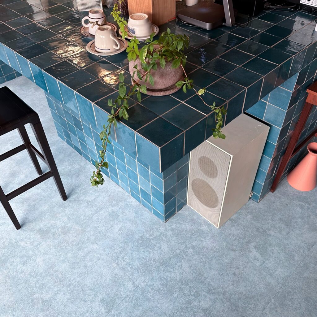 Blue tiled counter with a potted plant and cups, a black stool and a small speaker