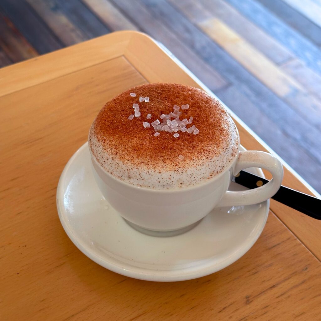 A cappuccino in a white cup with dusted foam and sugar crystals on top