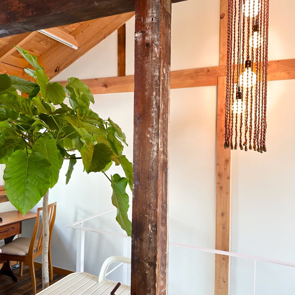 Second floor with a weathered wooden post and beams, a large green plant and a long beaded pendant lamp