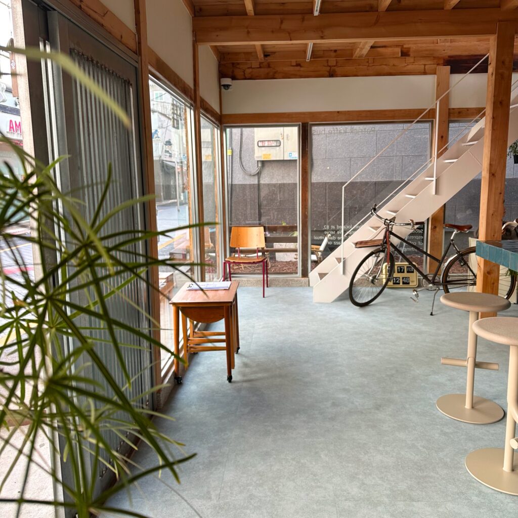 Bright first floor with a concrete floor, a white open staircase, a parked bicycle and wooden stools by the glass front